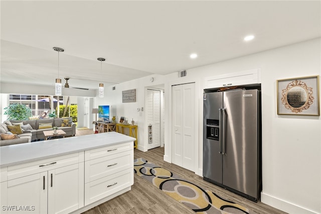 kitchen with stainless steel fridge, open floor plan, white cabinets, light countertops, and light wood-style floors