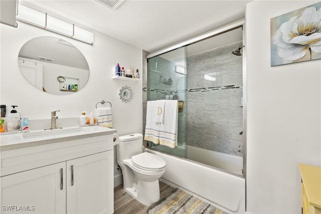 full bath with toilet, wood finished floors, visible vents, bath / shower combo with glass door, and vanity
