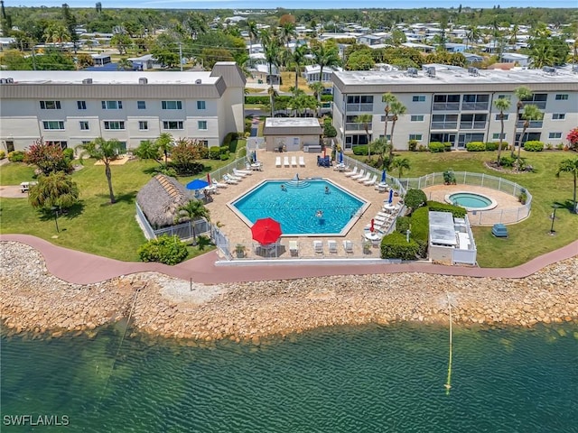 community pool featuring a patio, a fenced backyard, a lawn, a water view, and a hot tub