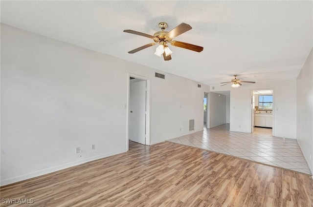empty room with a ceiling fan, light wood finished floors, and visible vents