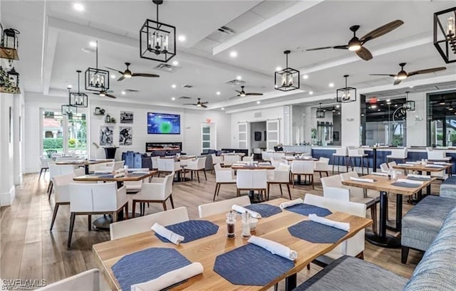 dining area featuring ceiling fan with notable chandelier, a tray ceiling, recessed lighting, and light wood-type flooring
