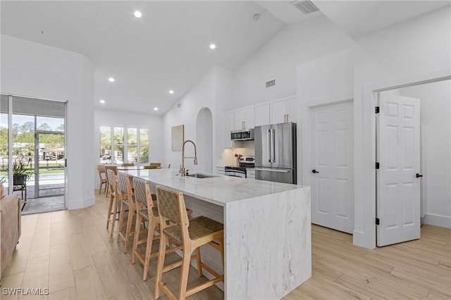 595 31st St NW, Naples, FL 34120 - kitchen with stainless steel appliances, a sink, arched walkways, white cabinetry, and light wood finished floors