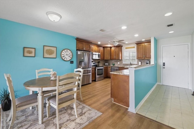 kitchen featuring a peninsula, visible vents, brown cabinets, decorative backsplash, and stainless steel appliances