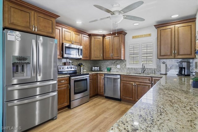kitchen with a sink, light stone countertops, a ceiling fan, and stainless steel appliances