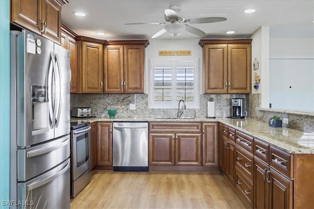 kitchen featuring ceiling fan, light stone countertops, a peninsula, appliances with stainless steel finishes, and a sink