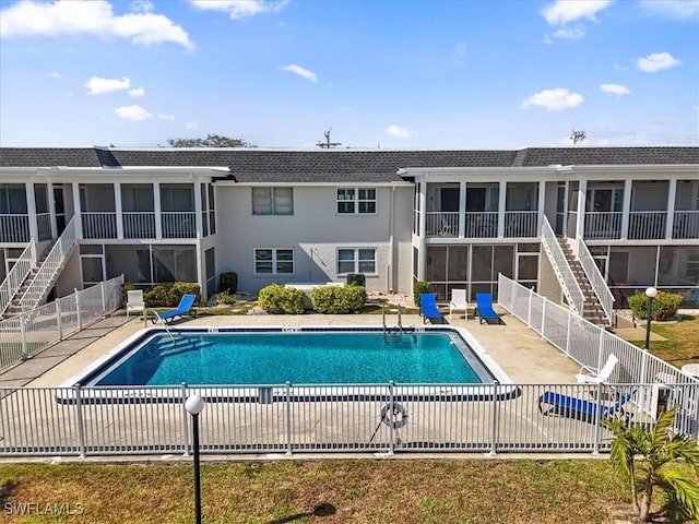 community pool featuring fence, a patio area, a sunroom, and stairs