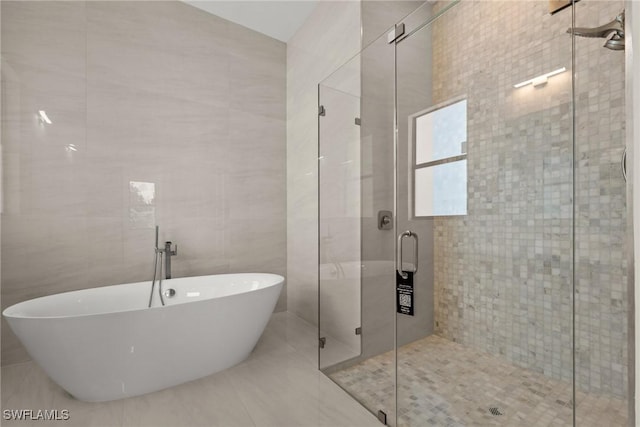 bathroom with tile walls, a freestanding tub, a stall shower, and tile patterned flooring
