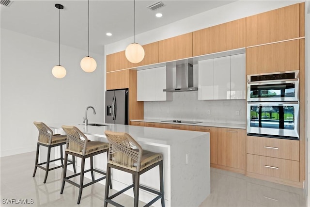 kitchen with appliances with stainless steel finishes, a sink, wall chimney range hood, light countertops, and a kitchen bar