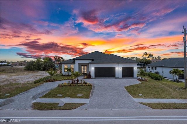 view of front of house featuring an attached garage, decorative driveway, stucco siding, and a yard
