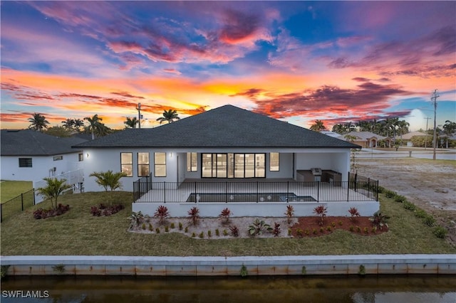 back of house at dusk with stucco siding and a shingled roof
