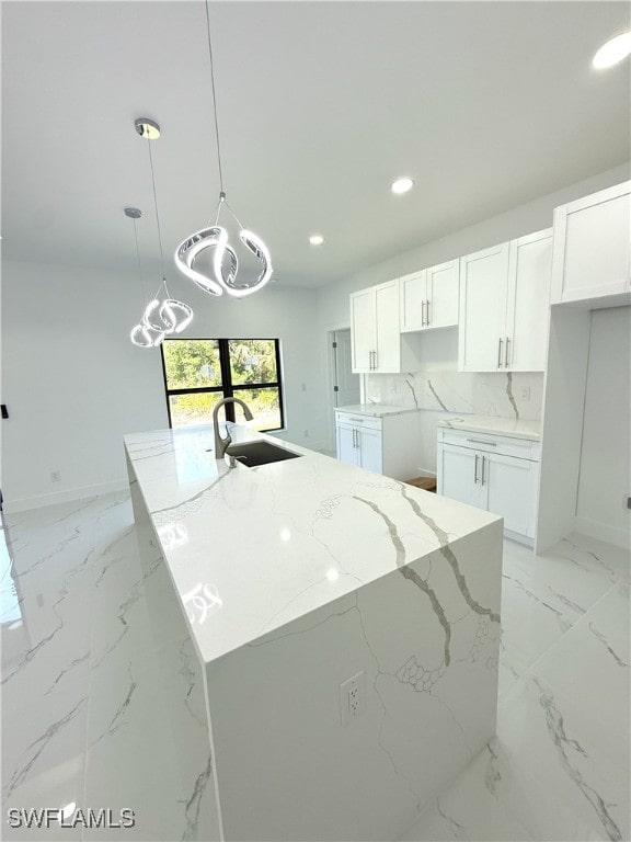 kitchen with white cabinetry, a chandelier, light stone counters, marble finish floor, and a sink