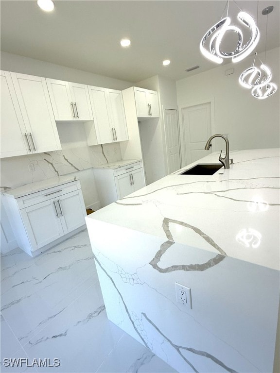 kitchen with light stone counters, recessed lighting, white cabinets, marble finish floor, and a sink