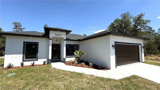 prairie-style house featuring concrete driveway, a front yard, a garage, and stucco siding
