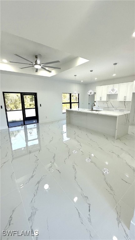 unfurnished living room featuring baseboards, a tray ceiling, marble finish floor, and a ceiling fan