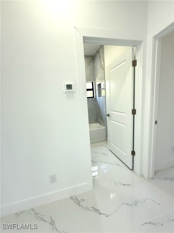 bathroom with a tub, marble finish floor, and baseboards