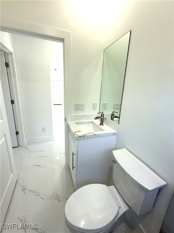 bathroom featuring toilet, marble finish floor, vanity, and baseboards