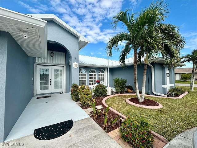 property entrance with french doors, metal roof, stucco siding, and a yard