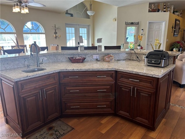 kitchen with dark wood-style flooring, a kitchen bar, a sink, and light stone counters