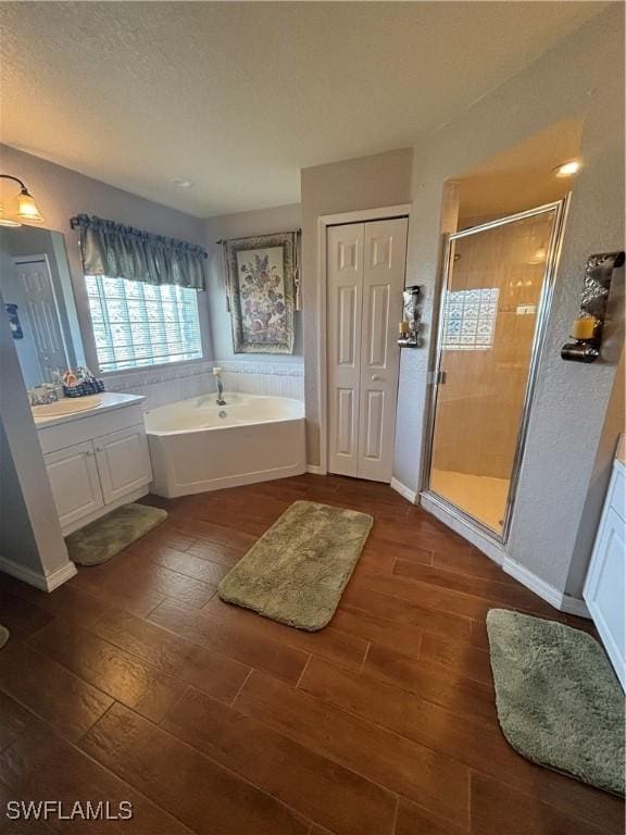 bathroom with a bath, a stall shower, wood finished floors, and vanity