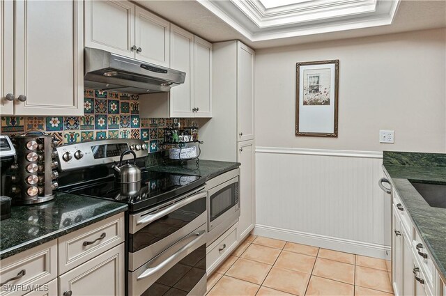4111 Gunnison Ct Unit 1212, Estero, FL 33928 - kitchen with under cabinet range hood, wainscoting, dark stone counters, stainless steel appliances, and light tile patterned flooring