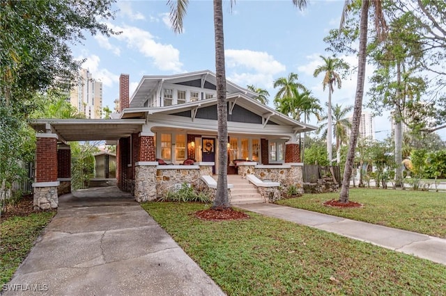 craftsman-style house with a chimney, a front lawn, driveway, covered porch, and an attached carport
