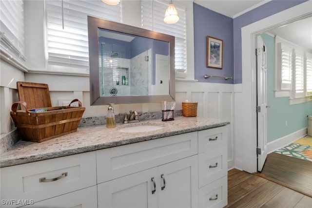 bathroom featuring a wainscoted wall, wood finished floors, vanity, and a stall shower
