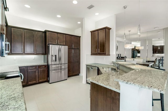 3267 Pacific Dr, Naples, FL 34119 - kitchen featuring appliances with stainless steel finishes, a sink, dark brown cabinets, a breakfast bar, and light stone countertops