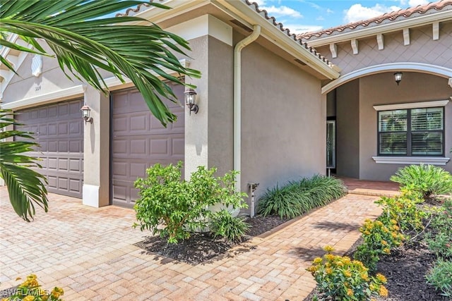view of exterior entry with stucco siding, an attached garage, and decorative driveway