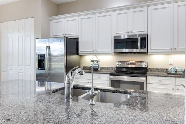 kitchen with white cabinets, stainless steel appliances, a sink, and dark stone counters