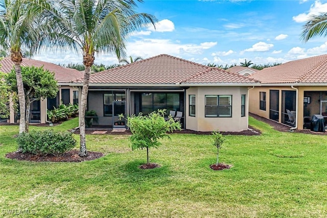 rear view of house featuring stucco siding, a tile roof, a sunroom, and a yard