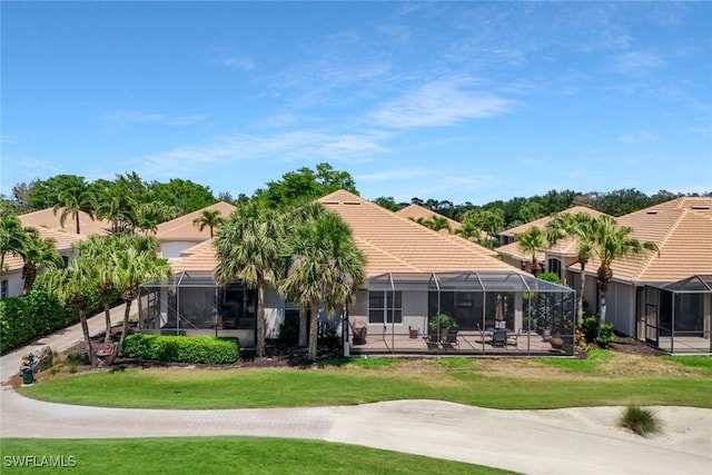 12732 Fox Ridge Dr, Bonita Springs, FL 34135 - rear view of house featuring a tile roof, glass enclosure, a lawn, and stucco siding