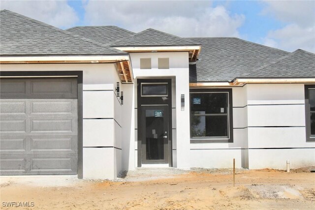 property entrance featuring a garage, roof with shingles, and stucco siding