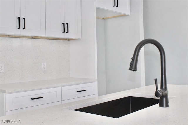 room details featuring white cabinetry, light stone countertops, and a sink
