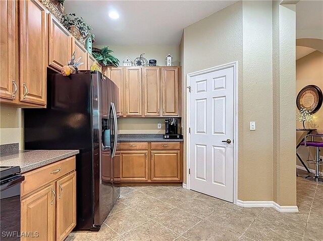 13885 Cleto Dr, Estero, FL 33928 - kitchen featuring range, light tile patterned floors, black fridge with ice dispenser, brown cabinetry, and arched walkways