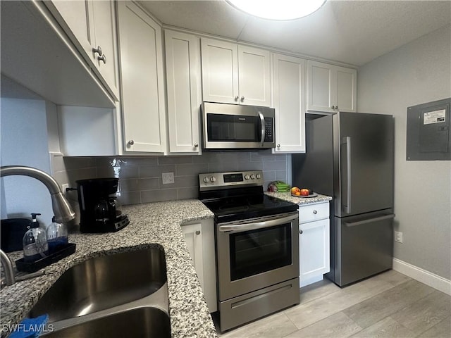 kitchen featuring white cabinets, electric panel, a sink, stainless steel appliances, and decorative backsplash