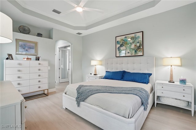 bedroom with arched walkways, a tray ceiling, visible vents, and light wood-style flooring