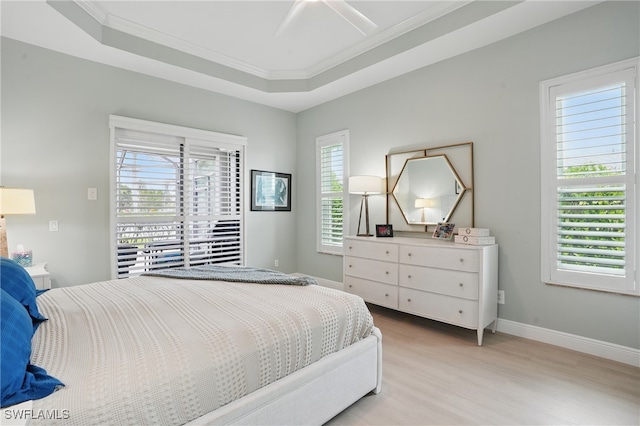 bedroom featuring crown molding, baseboards, light wood-style flooring, and a tray ceiling