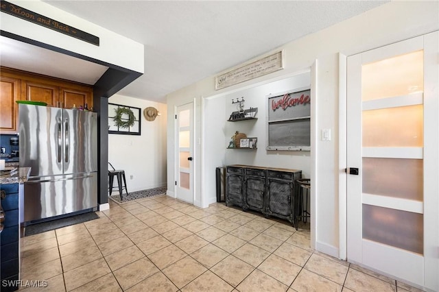 kitchen with brown cabinetry, light tile patterned floors, baseboards, and freestanding refrigerator