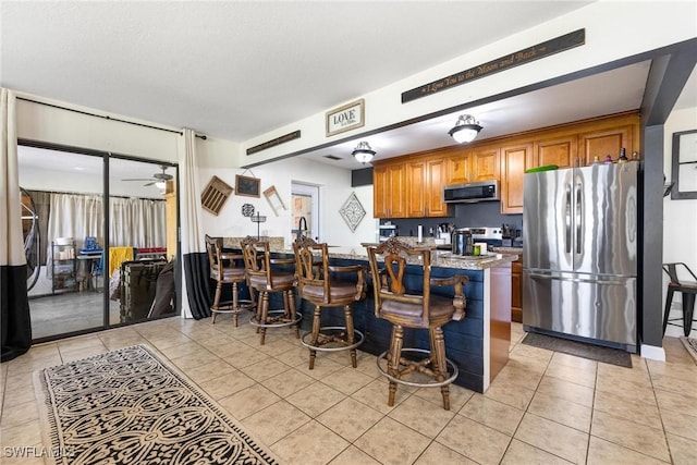kitchen featuring light tile patterned flooring, brown cabinets, ceiling fan, and stainless steel appliances