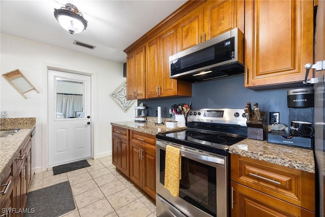kitchen with light stone counters, light tile patterned floors, visible vents, brown cabinetry, and appliances with stainless steel finishes