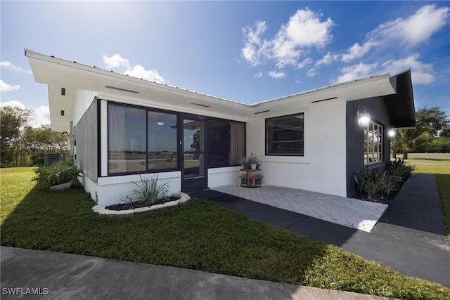view of front of house with a sunroom, stucco siding, and a front lawn
