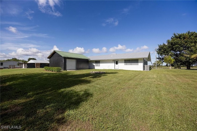 rear view of property featuring a garage, an outbuilding, metal roof, and a lawn