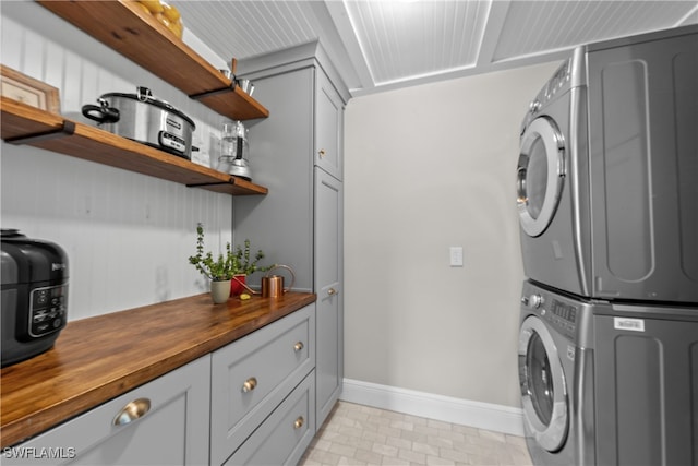 clothes washing area featuring stacked washing maching and dryer, baseboards, and cabinet space