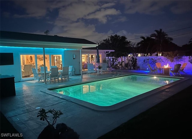 pool at night with a patio area, a fenced in pool, and fence