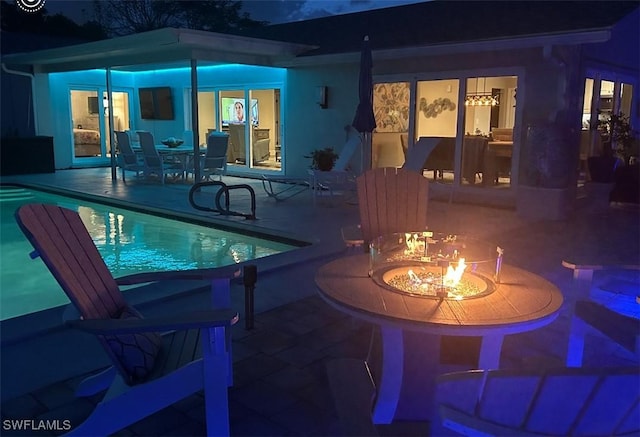 pool at night featuring an outdoor fire pit, a patio, and an outdoor pool