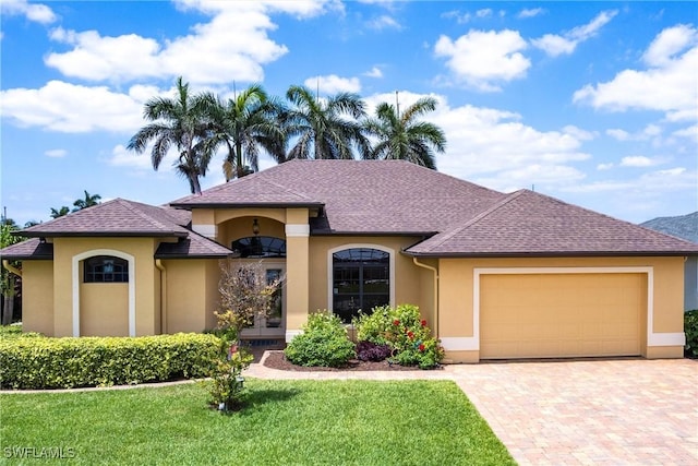 view of front of home with decorative driveway, a front yard, a garage, and stucco siding