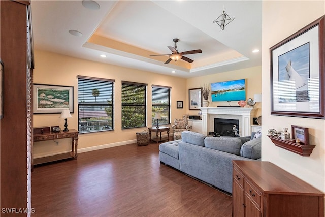 living room featuring a raised ceiling, ceiling fan, a glass covered fireplace, recessed lighting, and dark wood-type flooring