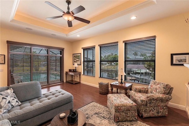 living area with baseboards, wood finished floors, and a tray ceiling
