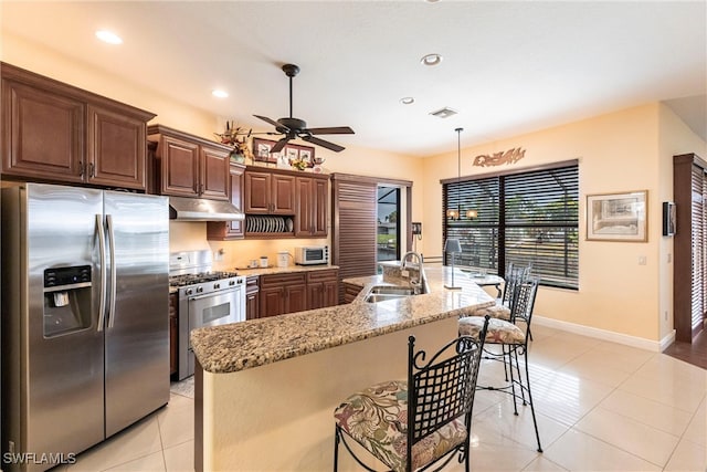 kitchen with a sink, under cabinet range hood, ceiling fan, a breakfast bar area, and appliances with stainless steel finishes