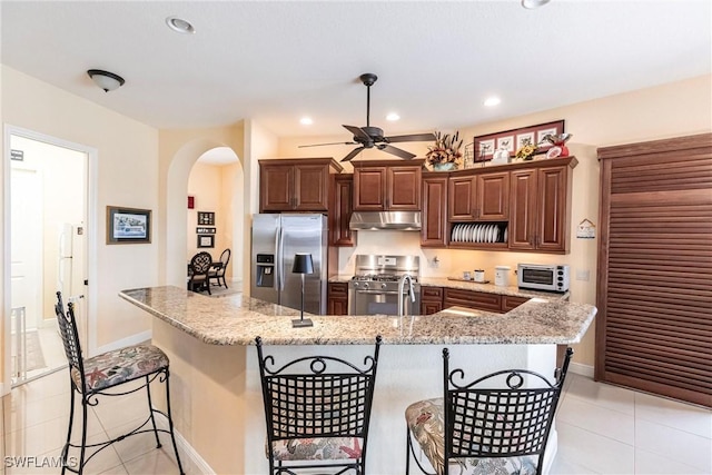 kitchen featuring appliances with stainless steel finishes, a breakfast bar, ceiling fan, arched walkways, and under cabinet range hood